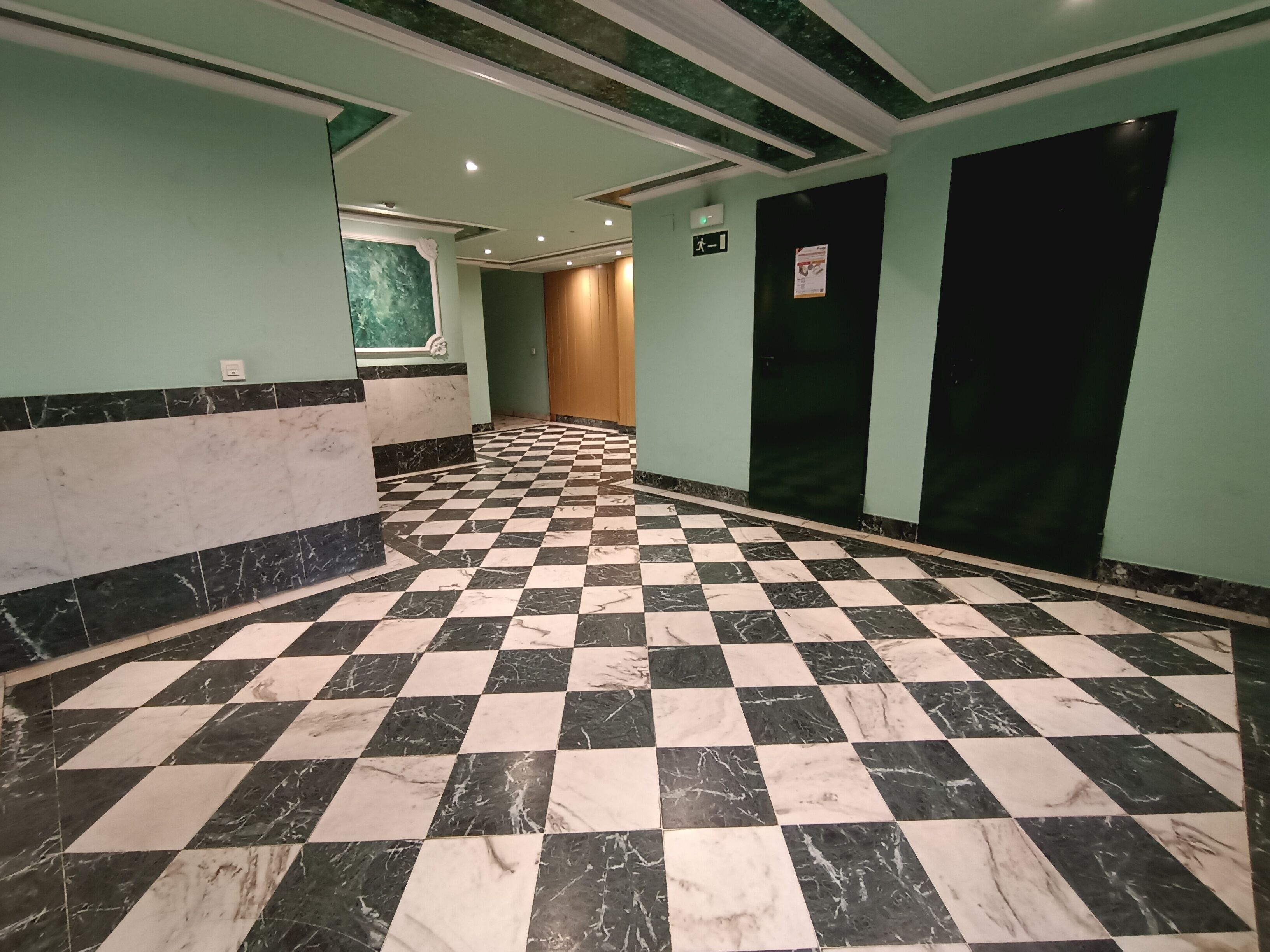 A hallway with a checkered floor, green walls, and a marble accent wall.