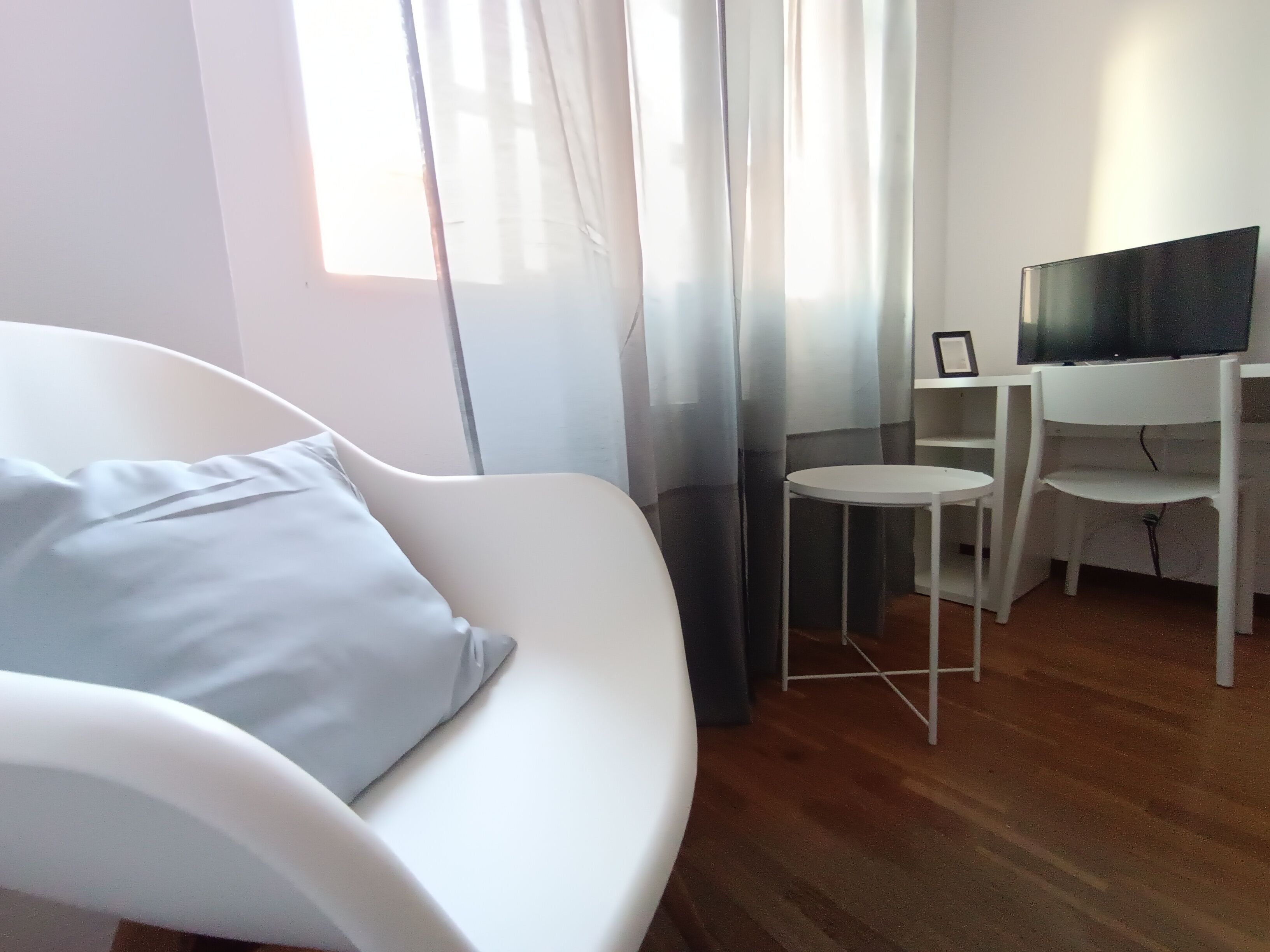 Una sala de estar moderna con un sofá blanco, una mesita redonda, un televisor sobre un mueble bajo y cortinas de gasa.