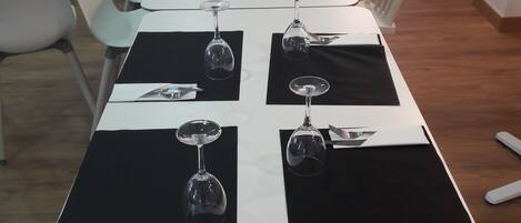 Una larga mesa de comedor con manteles individuales negros y copas de vino preparadas para una comida.