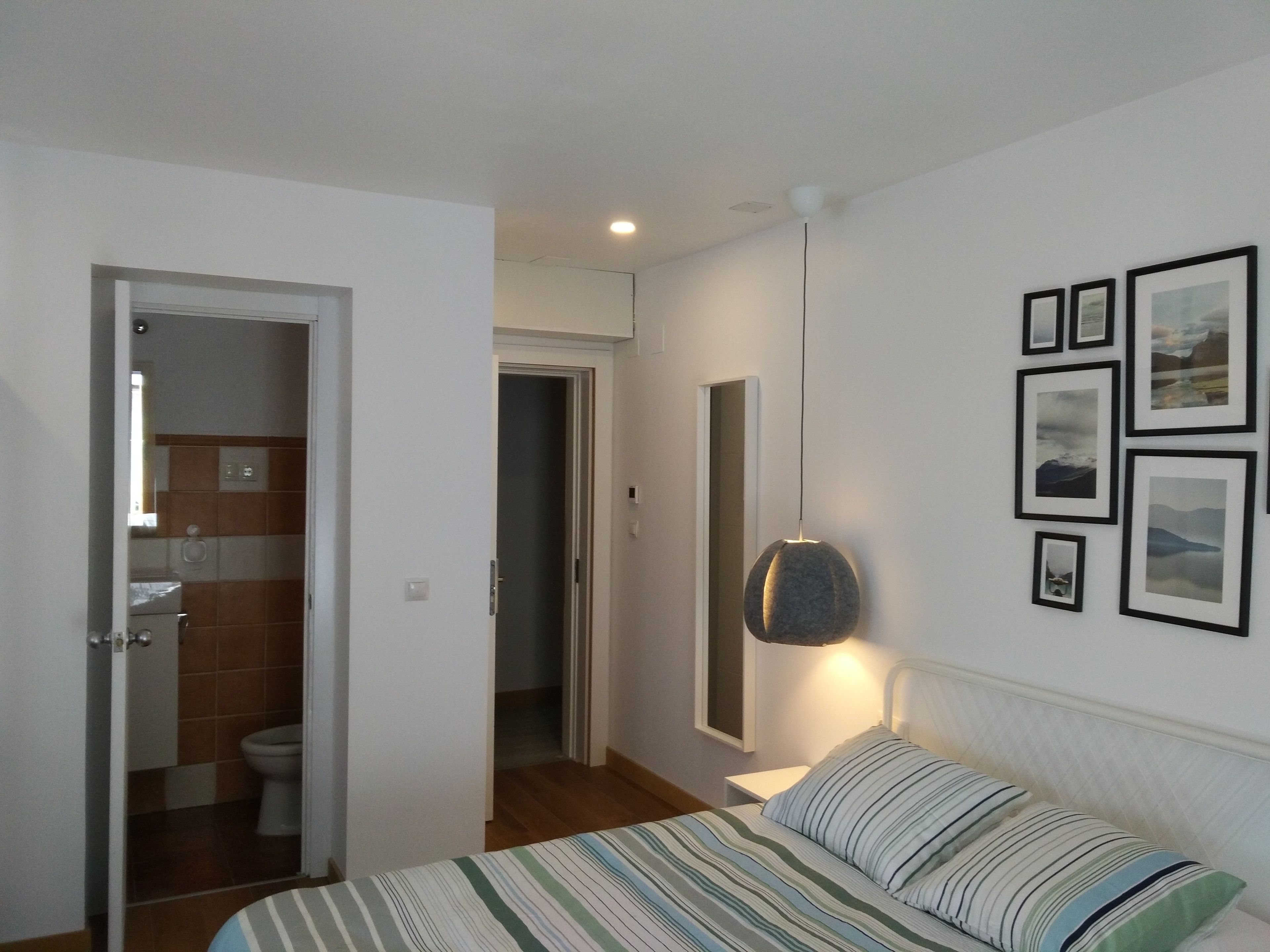 Un dormitorio con cama, mesita de noche, lámpara colgante y una pared decorada con cuadros.