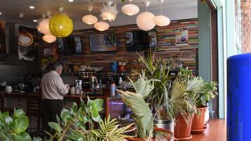 A restaurant interior with a bar area, potted plants, and hanging paper lanterns.