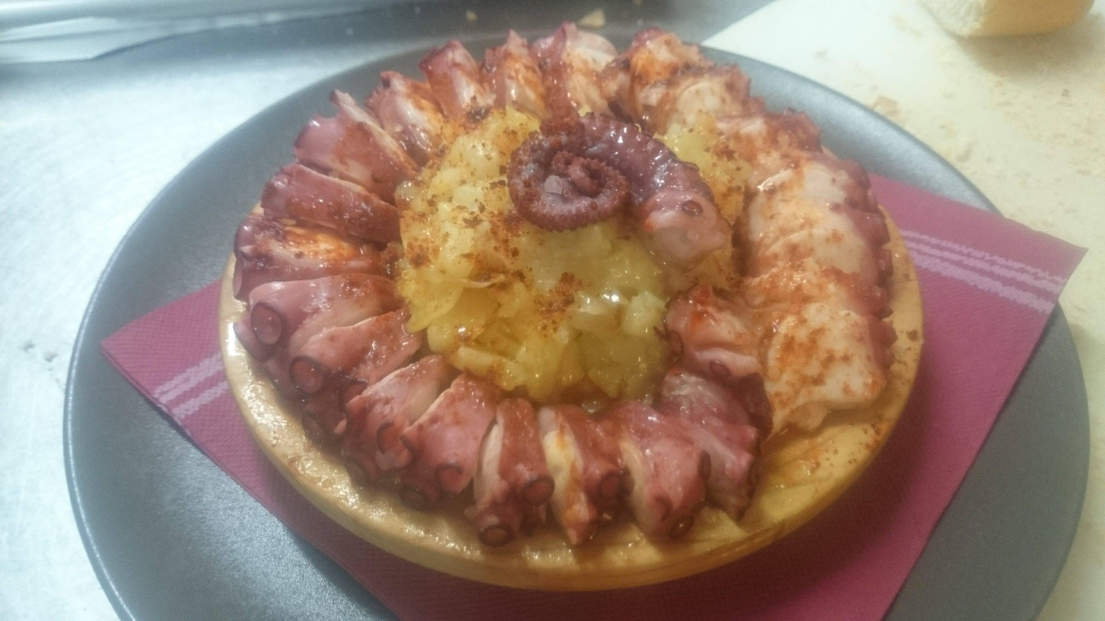 Un plato de pulpo con una guarnición central, servido sobre una mesa con un servilleta morada.