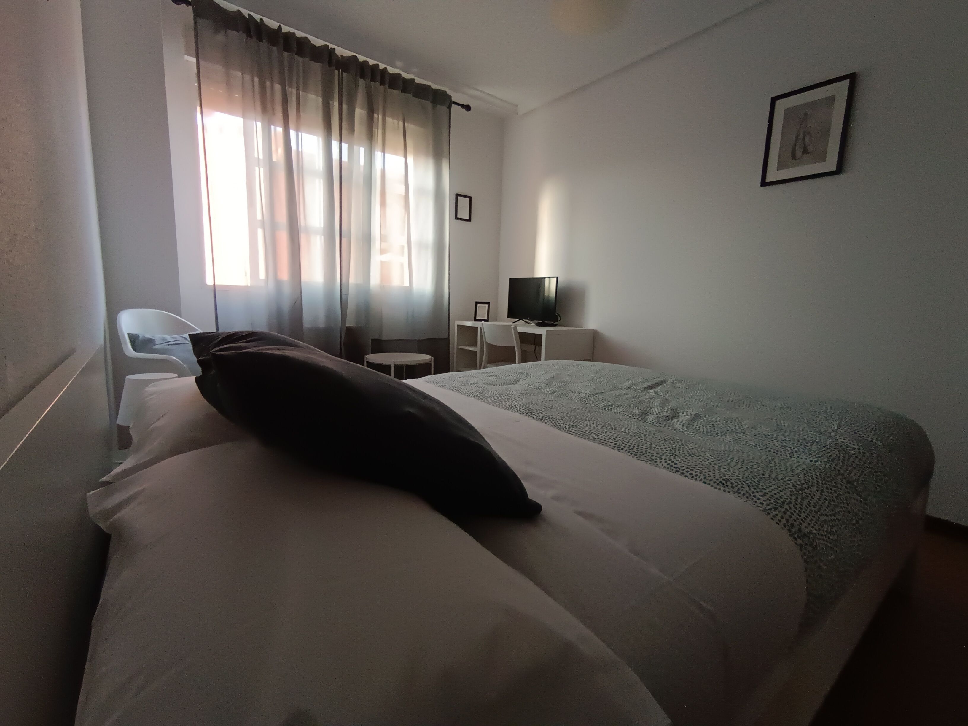 A hotel room with a bed, a desk, a chair, a TV, and a window with curtains.