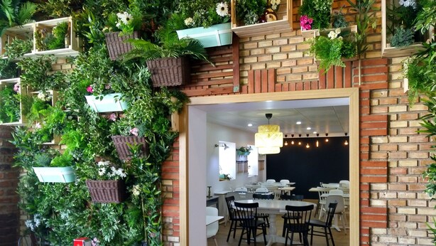 Ein Restaurant mit Backsteinwand und hängenden Pflanzen. Es gibt Tische und Stühle zum Essen.