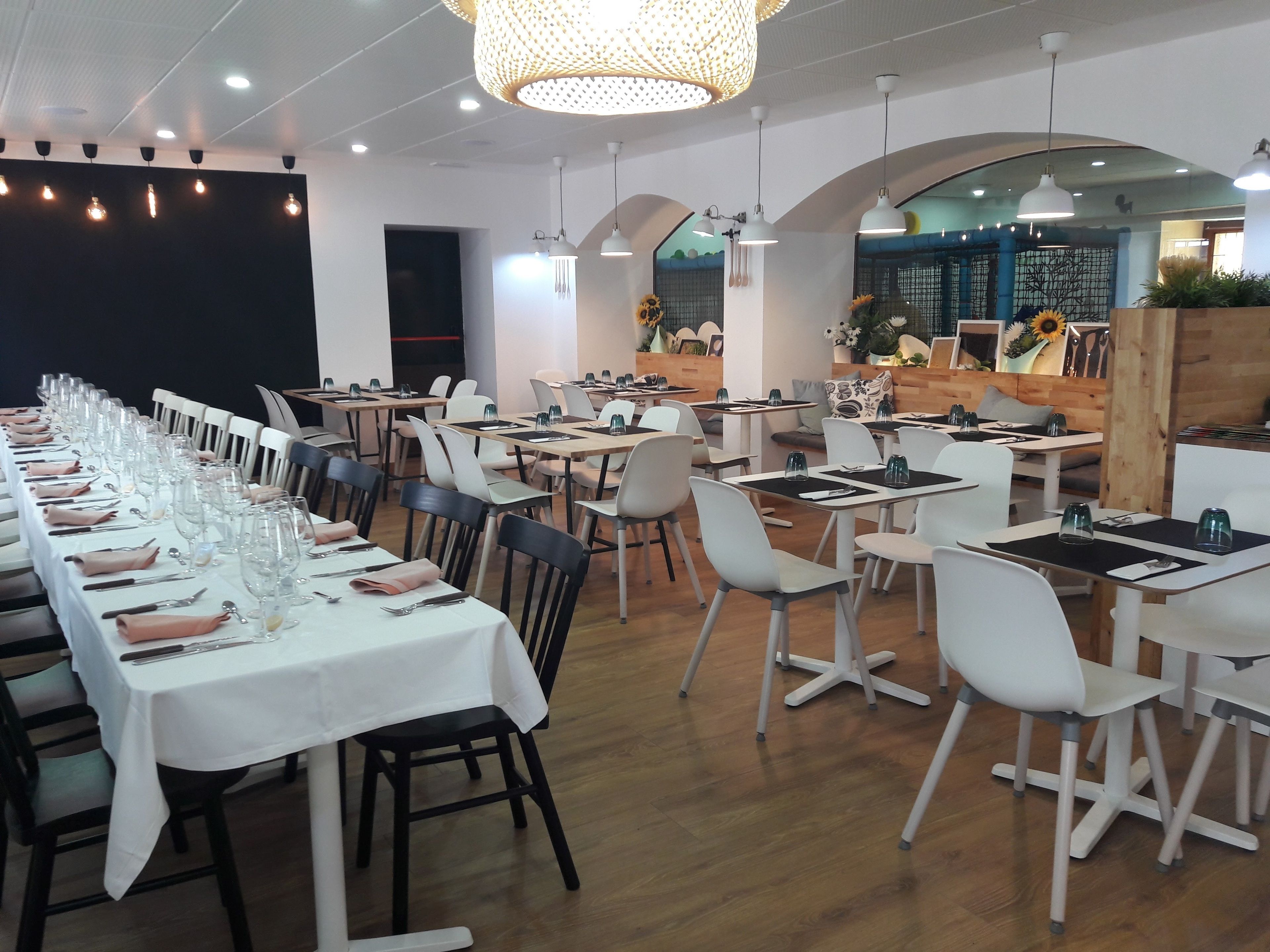 A restaurant with long tables set for dining, white chairs, and a modern interior design.