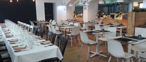 A restaurant with long tables set for dining, white chairs, and a modern interior design.