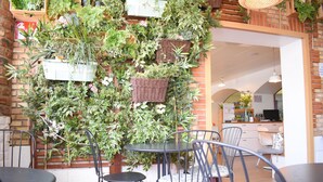 Ein Restaurant mit Außenbestuhlung, Korbmöbeln mit Pflanzen und einer Ziegelwand.
