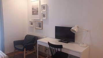 Ett litet, modernt rum med ett vitt skrivbord, en svart stol, en tv och en lampa.
