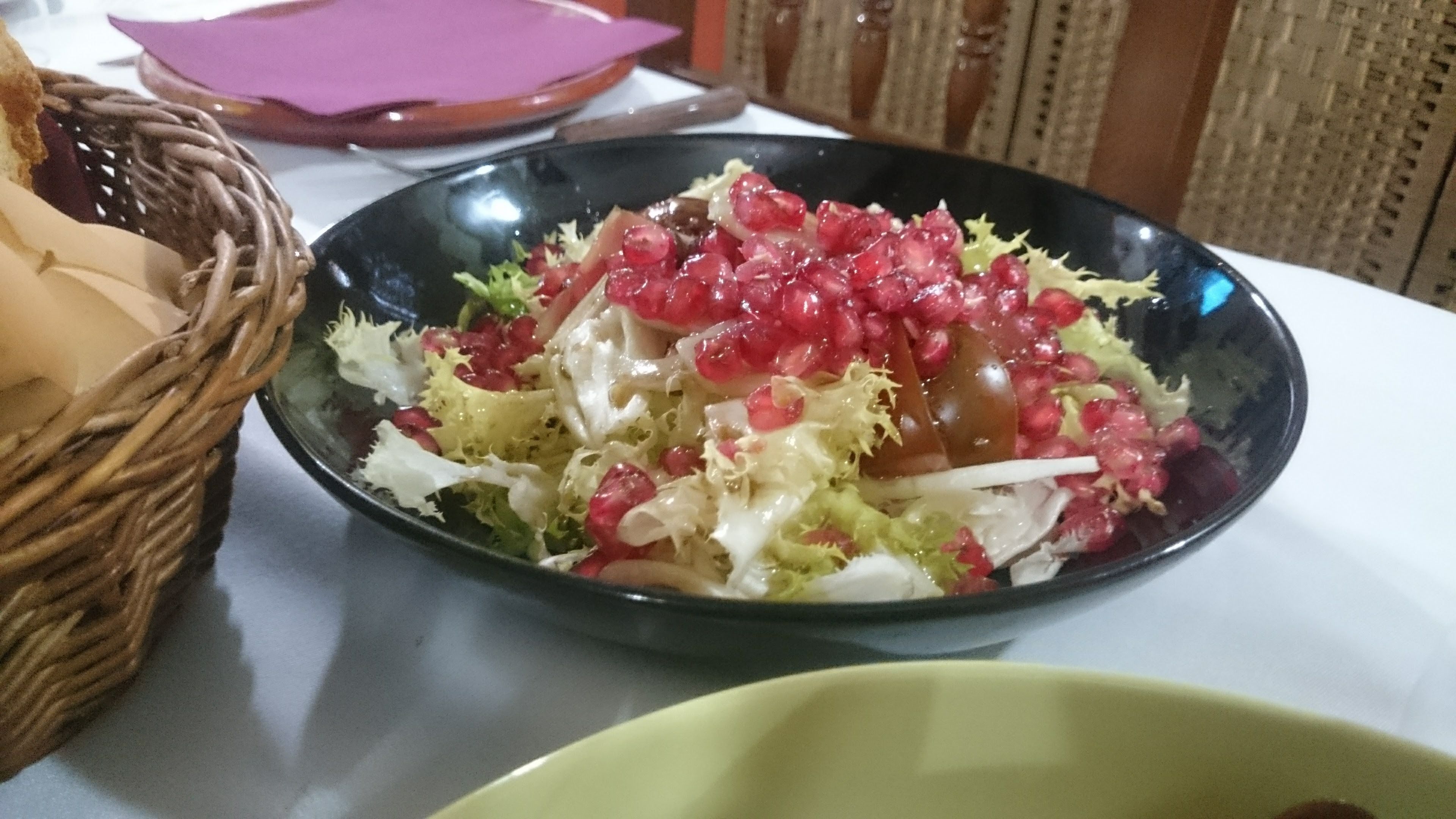 A salad with pomegranate seeds and lettuce in a black bowl on a table.