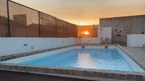 Ein rechteckiger Pool mit Steinbord, umgeben von einer weißen Mauer und einem Zaun.