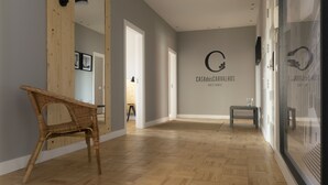 Ein moderner Hotelkorridor mit Holzböden, einem Korbsessel, einer Wandleuchte und einer Glastür mit einem Logo.