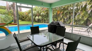 A patio area with a glass table and chairs, a ceiling fan, and a view of a swimming pool and greenery. - Tropical Getaway!!!! (Jensen Beach)