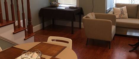 A dining area with a table set for four, a sofa, and a staircase.