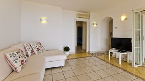 A living room with a sofa, a television, and a small table. There is a door leading to another room. - Beautiful View, Pool ,two steps from city center !! (Taormina)