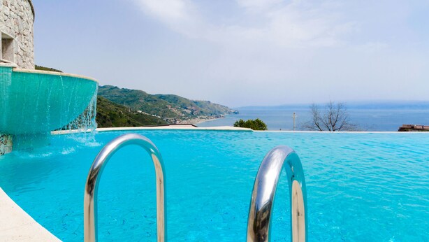 A clear blue pool with metal railings, overlooking a coastal landscape with hills and a view of the sea. - Beautiful View, Pool ,two steps from city center !! (Taormina)