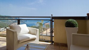 A balcony with a white sofa, a potted plant, and a view of a coastal landscape. - Beautiful View, Pool ,two steps from city center !! (Taormina)