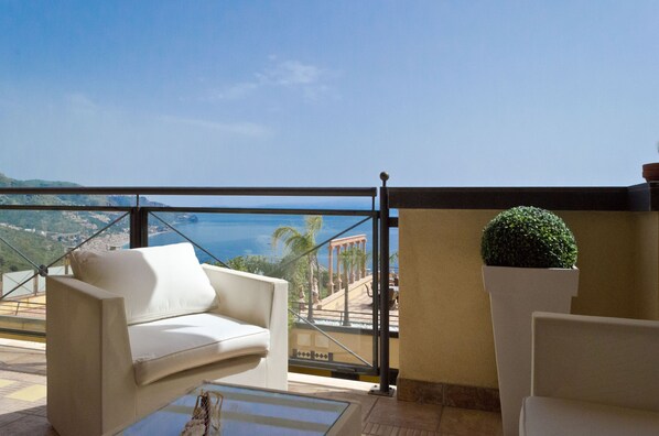 A balcony with a white sofa, a potted plant, and a view of a coastal landscape. - Beautiful View, Pool ,two steps from city center !! (Taormina)
