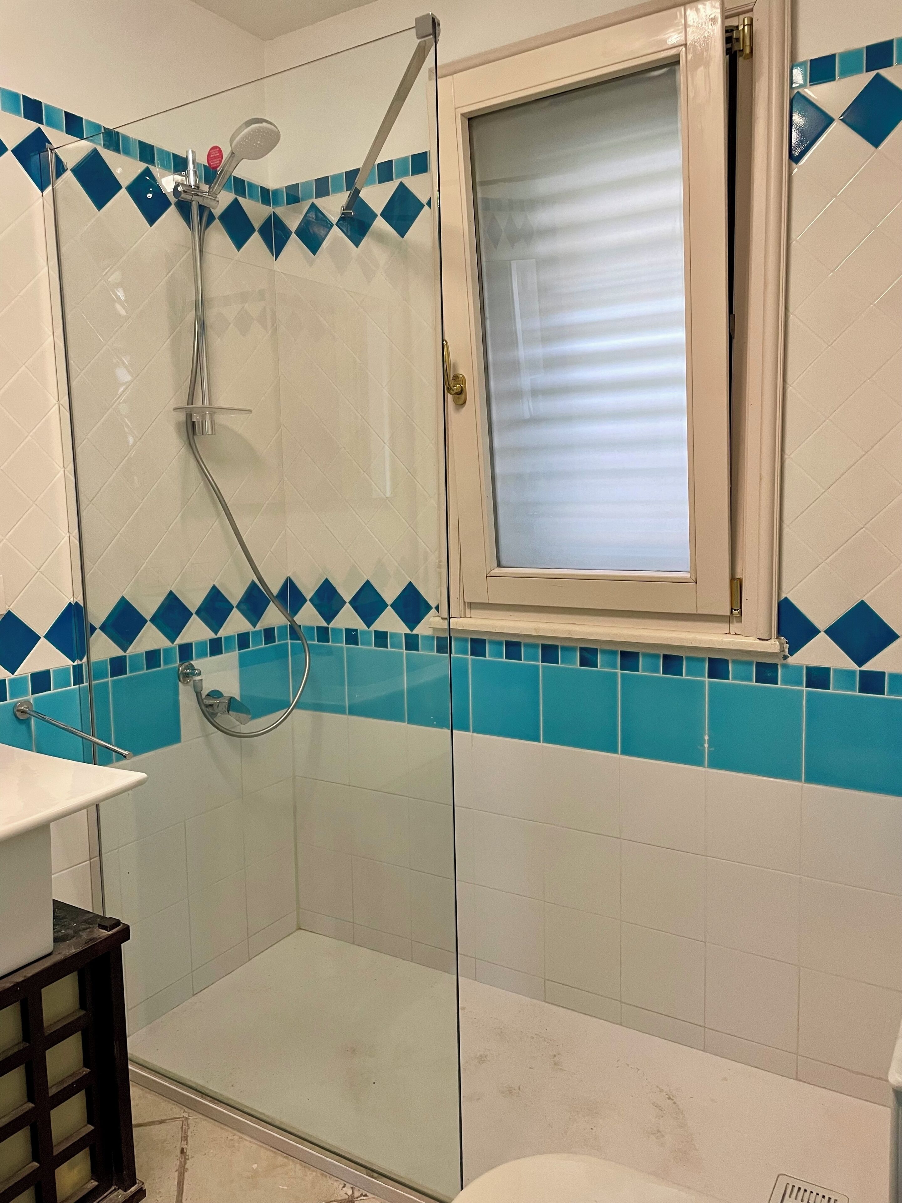 Un baño con cabina de ducha de vidrio, una ventana y paredes con azulejos azules.