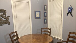 A dining room with a round wooden table, four wooden chairs, and a blue upholstered chair. There are three framed pictures on the wall and a decorative dragon on the left. - Pegasus Lair Upper Floor Apt.NoPetFee, NoChores.Short Walk to Satellite Venue! (Memphis)
