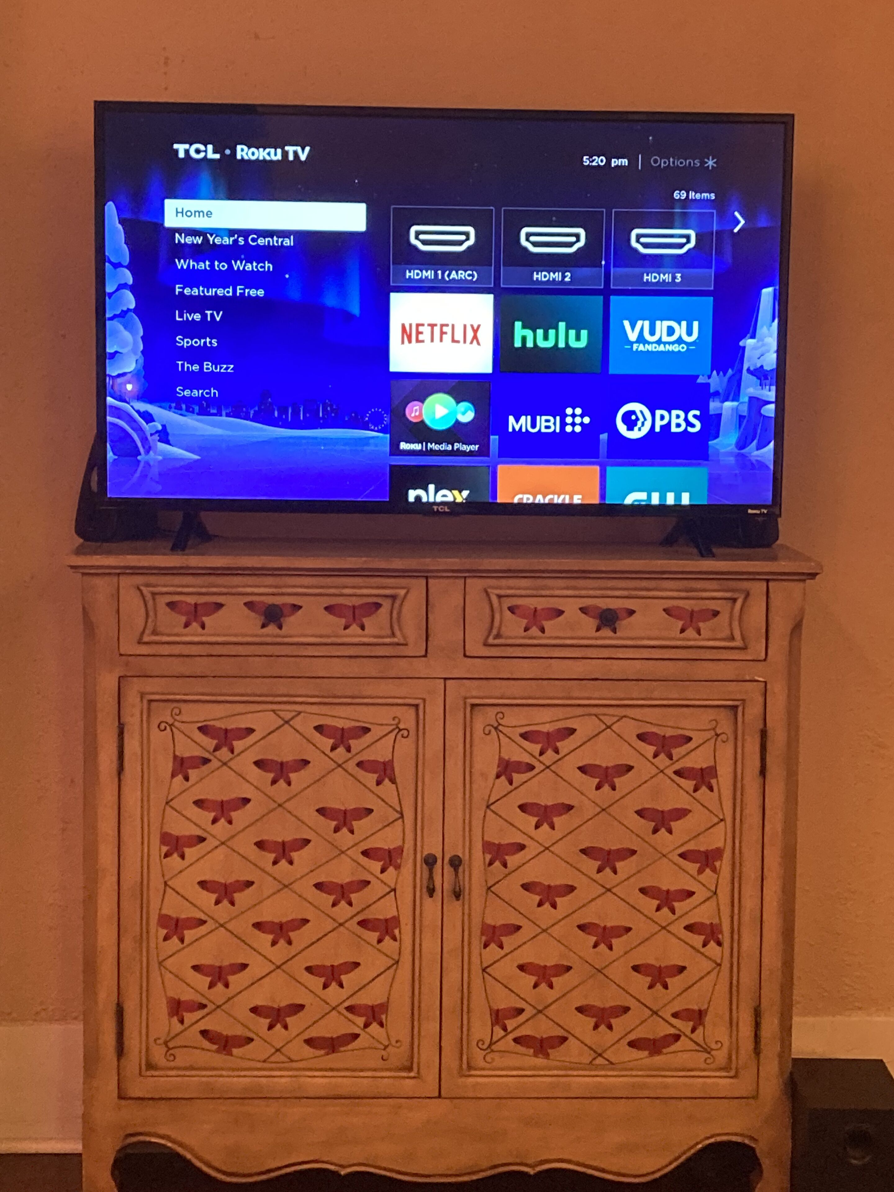 Un televisor TCL Roku sobre un mueble de madera con diseños de mariposas.