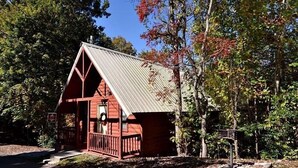 A small, red wooden cabin with a metal roof, surrounded by trees and a clear sky. - Gatlinburg Cabin Free Tickets, Heart Whirlpool, Hot Tub, King Bed, Fast Internet (Gatlinburg)