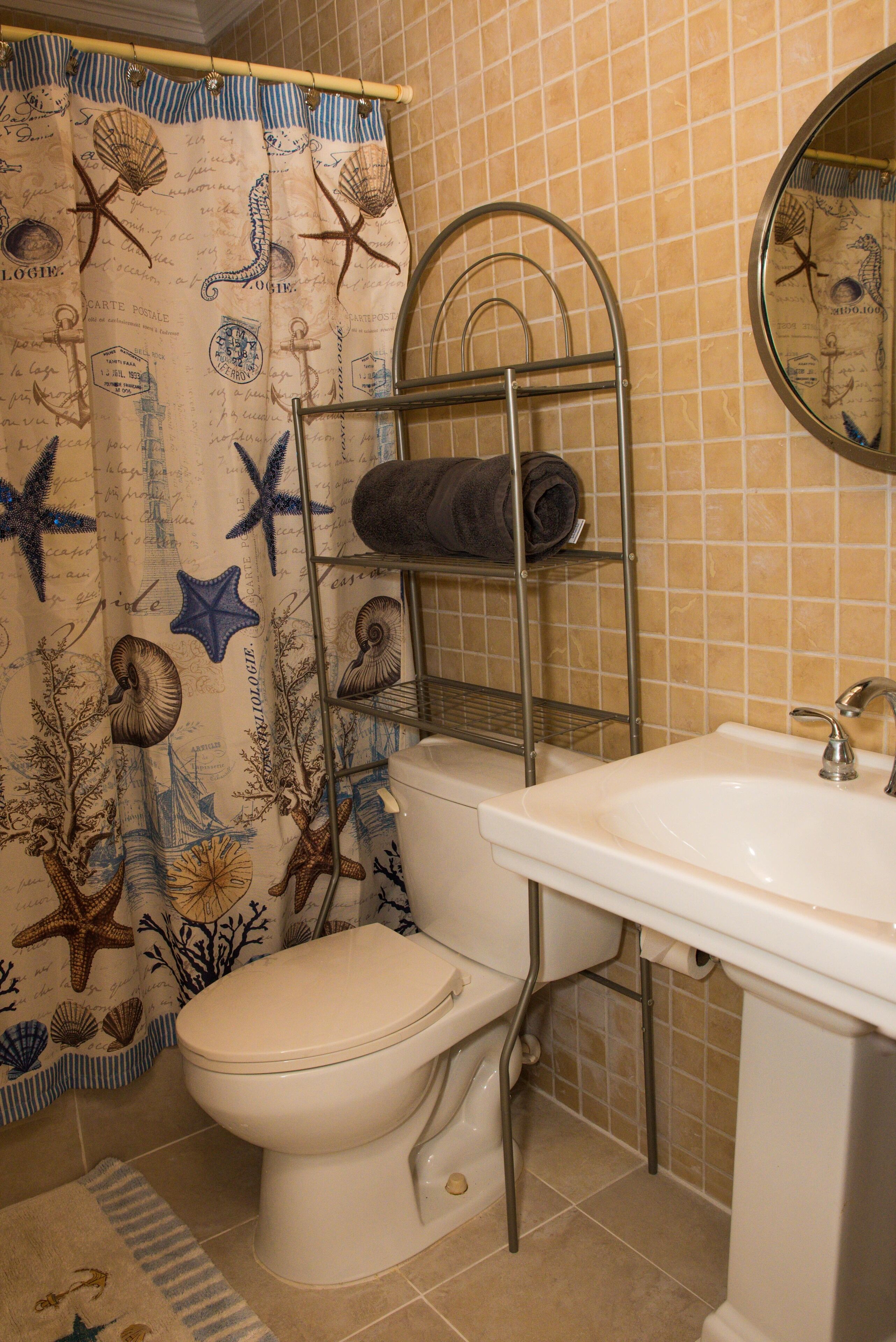 A bathroom with a toilet, a sink, a metal towel rack, and a shower curtain with sea-themed designs.