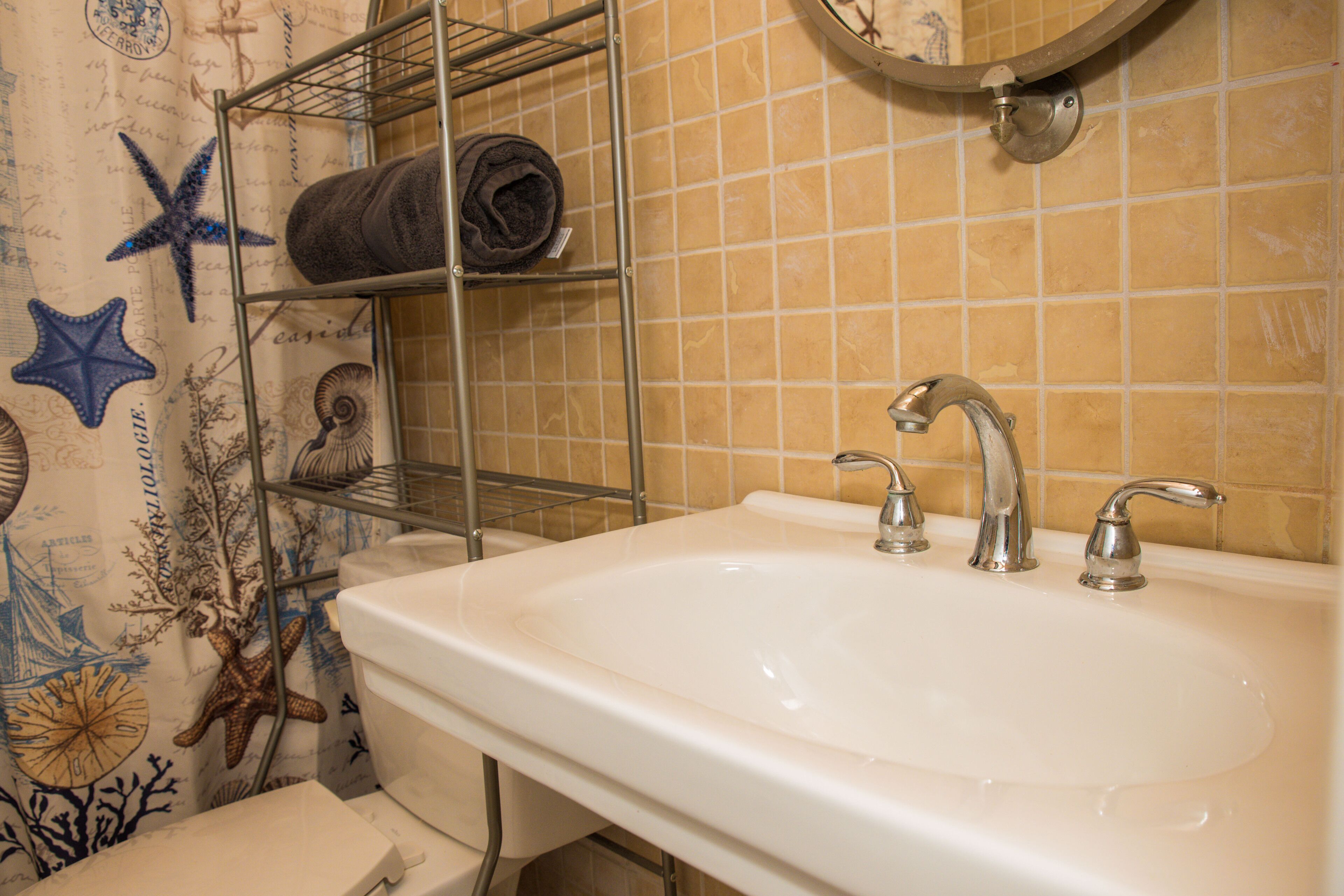 A bathroom with a white sink, two faucets, and a towel rack with a rolled towel.