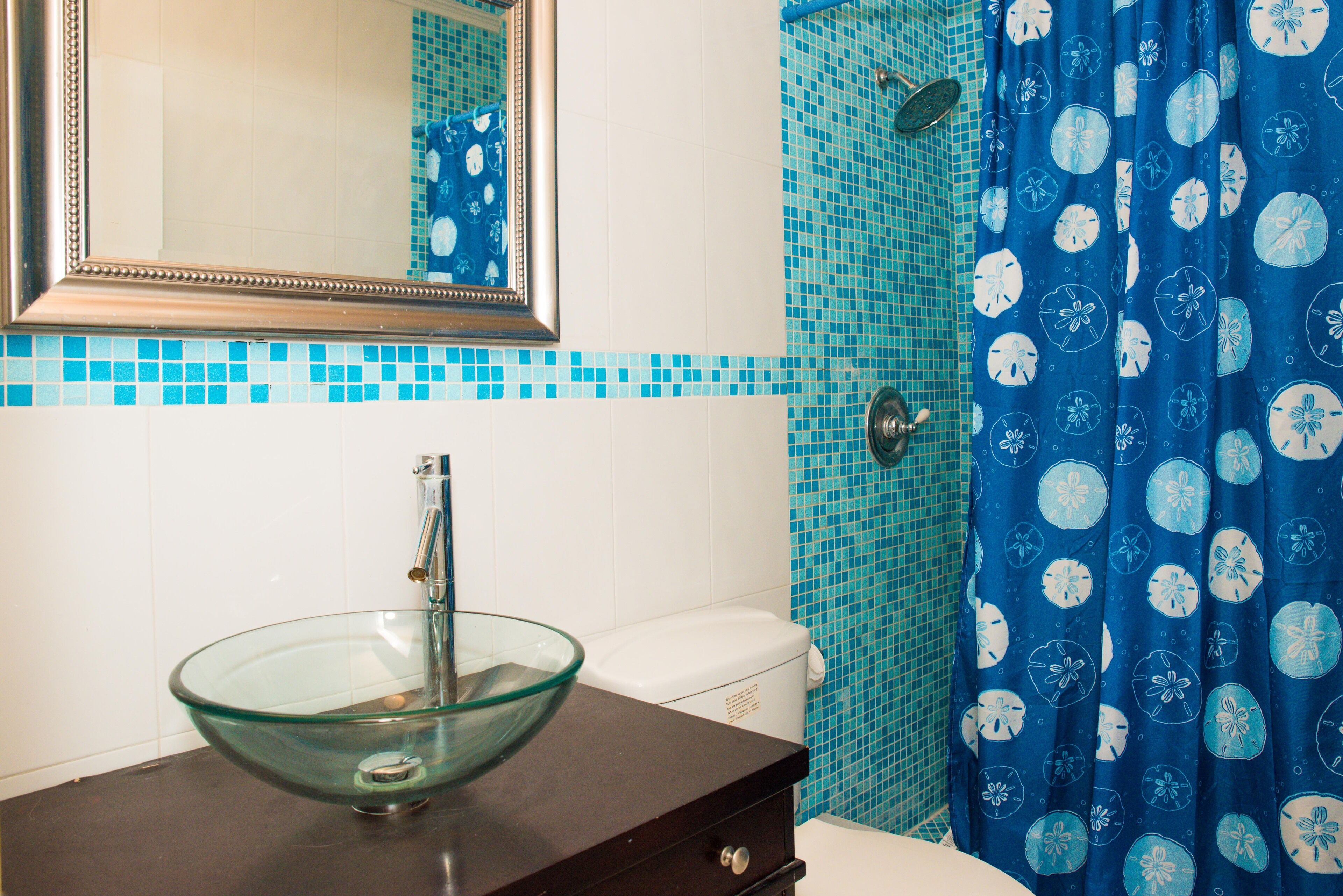 Un baño con lavamanos de cristal, inodoro blanco y ducha con cortina azul.