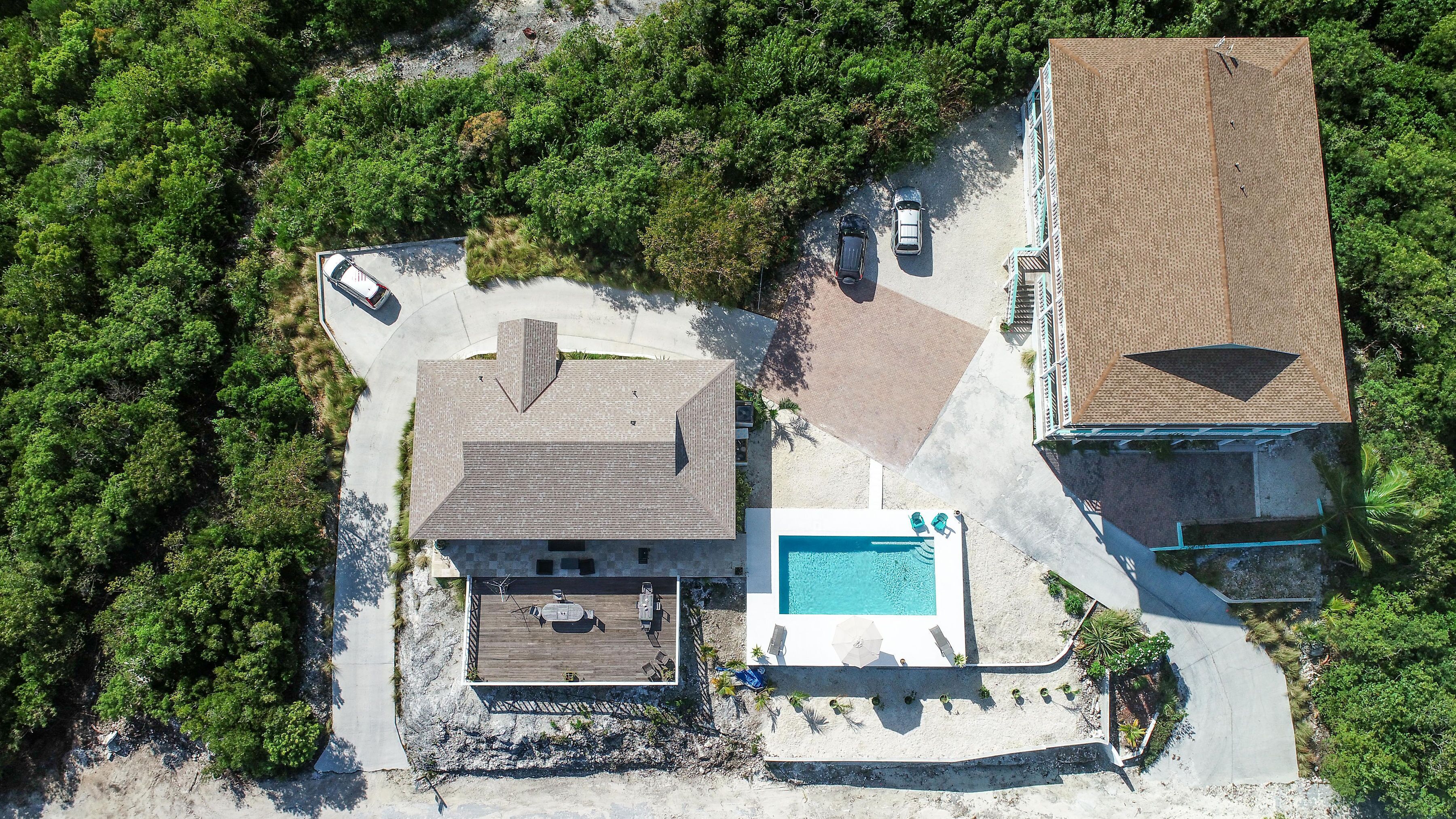 An aerial view of a property with a swimming pool, a covered patio, and a large house with a sloped roof.