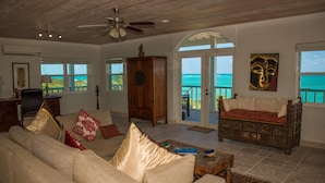A spacious living room with a beige sofa, a wooden cabinet, and a view of the ocean through large windows.