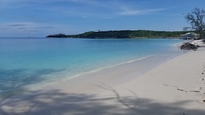 A beach with clear turquoise water, white sand, and a small island with greenery in the background.