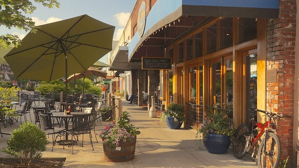An outdoor café with tables and chairs, potted plants, and a bicycle parked outside.