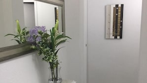 Un pasillo con una consola blanca, un espejo y un florero con flores.