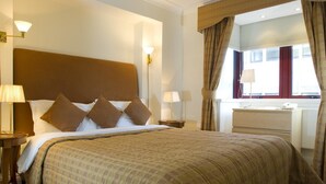 A hotel room with a large bed, two bedside tables with lamps, a dresser, and a window with curtains.