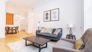 A modern living room with a sofa, armchair, coffee table, and two lamps. There is a dining area with a table and chairs.