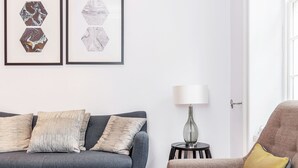 A modern living room with a grey sofa, a brown armchair, and a small side table with a lamp. There are two hexagonal wall art pieces above the sofa.