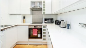 A modern kitchen with white cabinetry, a built-in oven, a microwave, and a kettle.