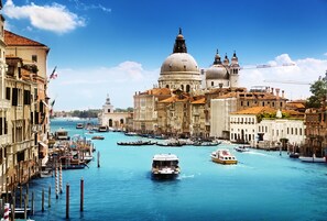 Un canal en Venecia con góndolas y barcos, edificios históricos y una estructura cúpula destacada.