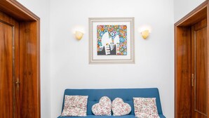 Une pièce avec un canapé bleu, des coussins à motifs floraux, un tableau encadré et des portes en bois.