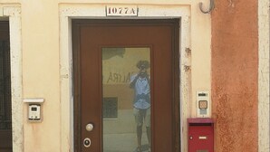 Une entrée d’immeuble avec une enseigne indiquant « RUGA BELLA » et une porte portant le numéro « 1077A ».