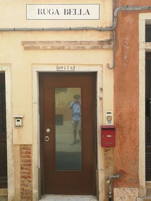 Entrada de edifício com placa indicando "RUGA BELLA" e porta com a inscrição "1077A".