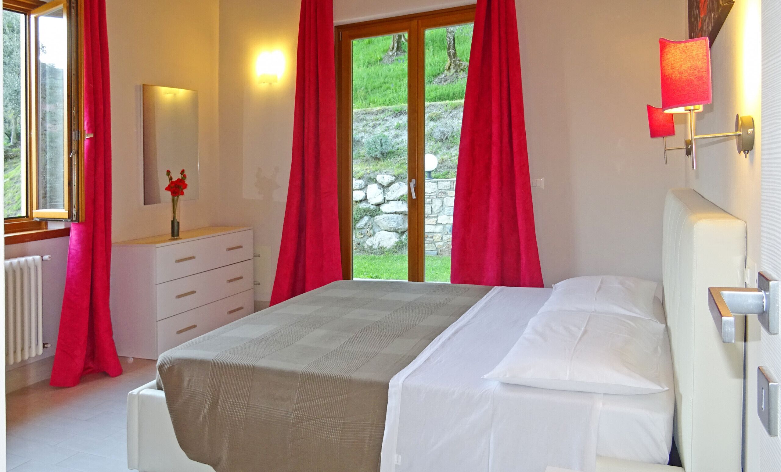 A bedroom with a bed, a dresser, a mirror, and a window with curtains.