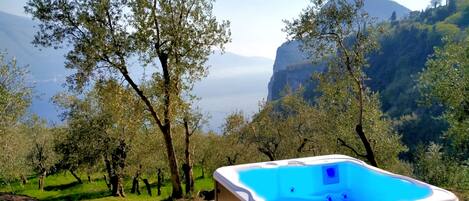 A hot tub on a wooden deck with a view of a mountainous landscape and trees.