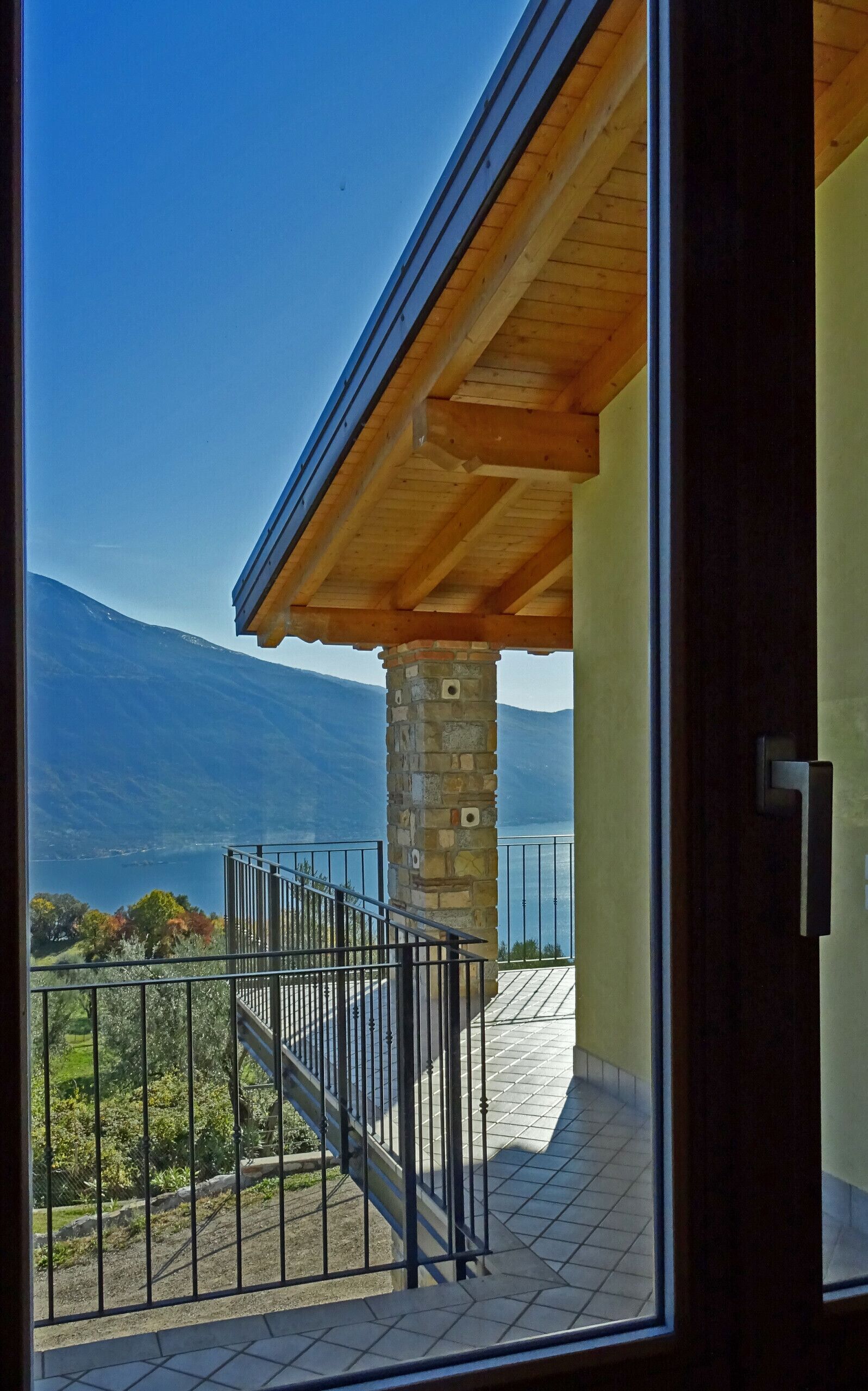 Ein Balkon mit Steinpfeiler, Holzdach und Blick auf Berg und See.