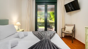 A hotel room with a bed, a TV mounted on the wall, a chair, and a view of the outdoors through a door. - El Rincon del Golf I - Isla Canela Golf GRHI6P06 (Isla Canela)