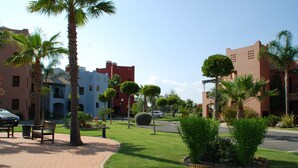 A paved walkway with benches, palm trees, and a well-maintained lawn. - El Rincon del Golf I - Isla Canela Golf GRHI6P06 (Isla Canela)