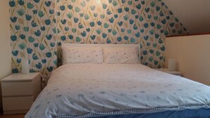 A bedroom with a bed, nightstands, and a wall with floral wallpaper. - Lavender gite Le Cosquer St Connec (Saint-Connec)