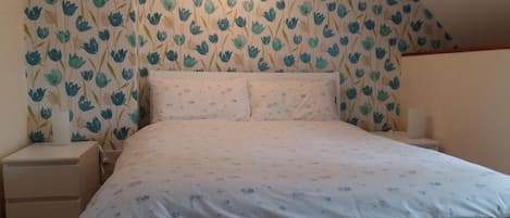 A bedroom with a bed, nightstands, and a wall with floral wallpaper.
