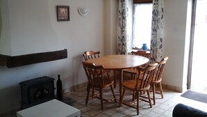 A dining area with a round wooden table and six chairs, a small black stove, and a white cabinet. - Lavender gite Le Cosquer St Connec (Saint-Connec)