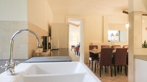 A modern kitchen with a large sink, a coffee machine, and a dining area with red chairs and a table.